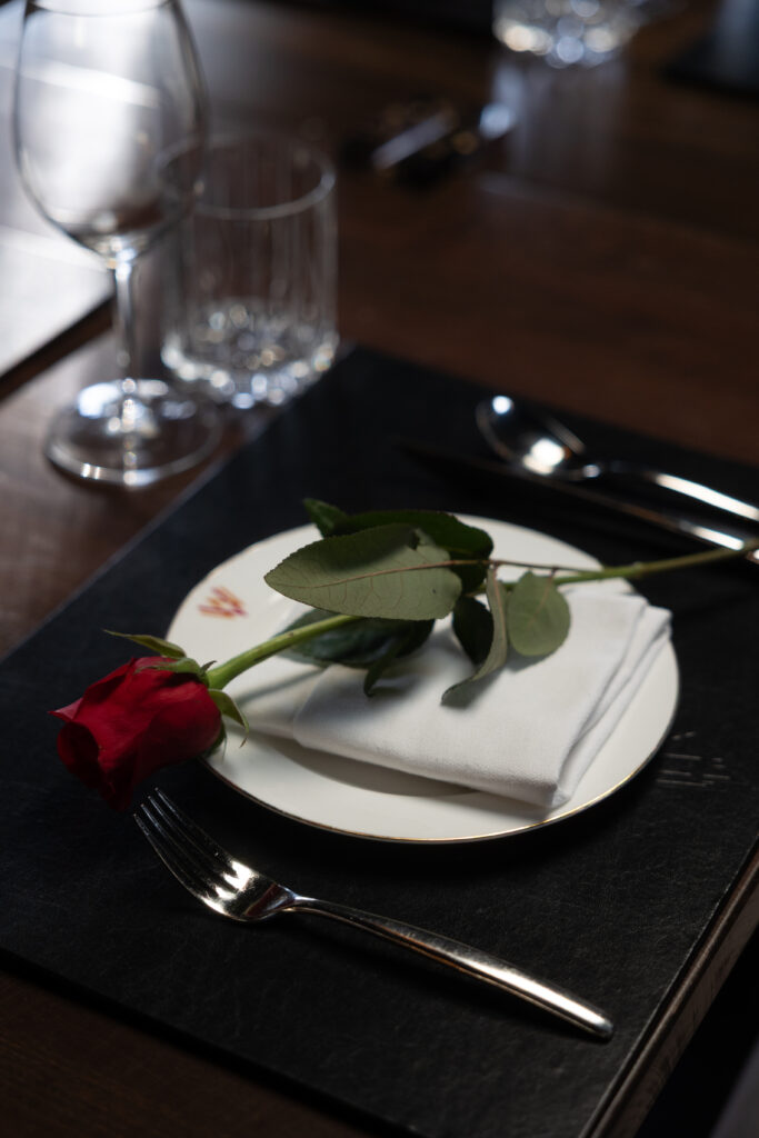 Single Red Rose On A White Napkin Atop A Fine China Plate At An Elegant Valentine'S Day Dinner Setting