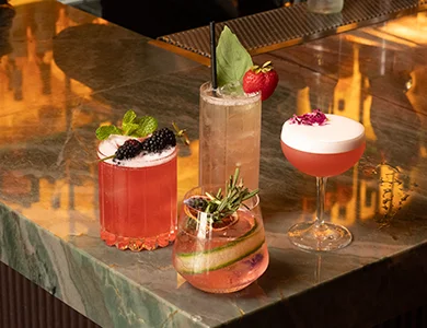 Three cocktails on a marble bar top in front of the wine wall at WeVINO