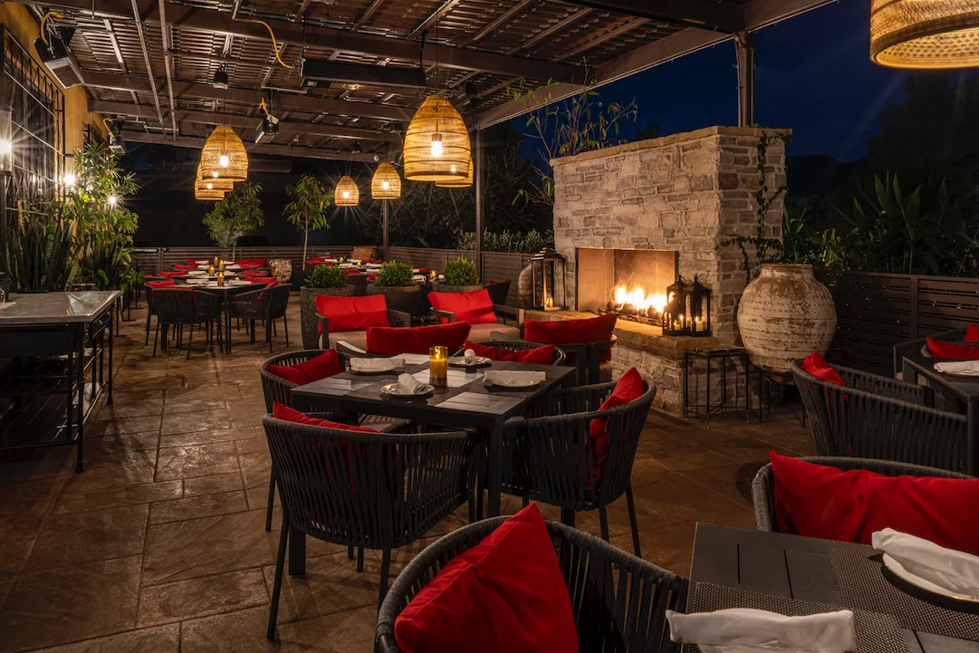 Covered patio at WeVINO with a stone fireplace, lanterns and red dining chairs