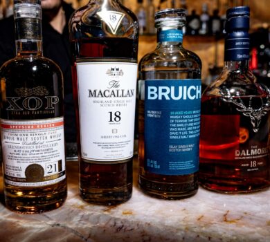 Image of four rare Scotch whisky bottles from Glenrothes, Macallan, Bruichladdich, and Dalmore displayed on a table at WeVINO in Westlake Village, set in a warm, candlelit ambiance.